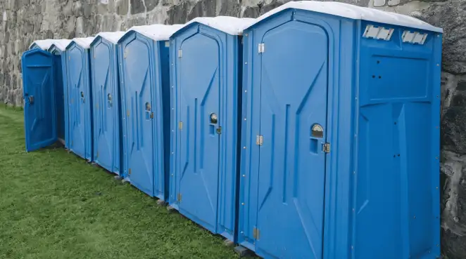 Row of blue portable toilets lined up on grass against a stone wall for event sanitation in Jackson, MS