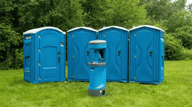 Four blue portable toilets and a matching hand washing station on grass near trees, a common sight at local outdoor events in Jackson, MS