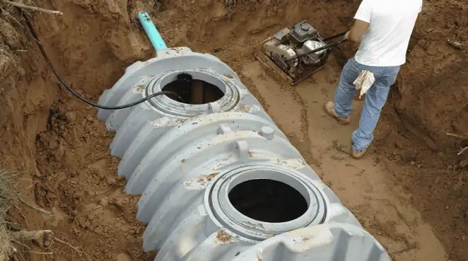 Septic tank installation showing a technician compacting soil around a new poly septic tank in an excavation pit in Jackson, MS